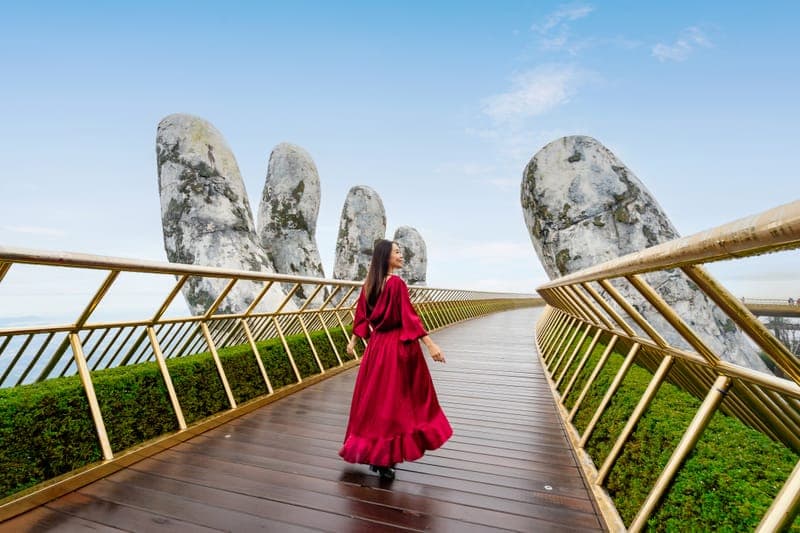 Visitor walking across the Golden Bridge held by giant stone hands